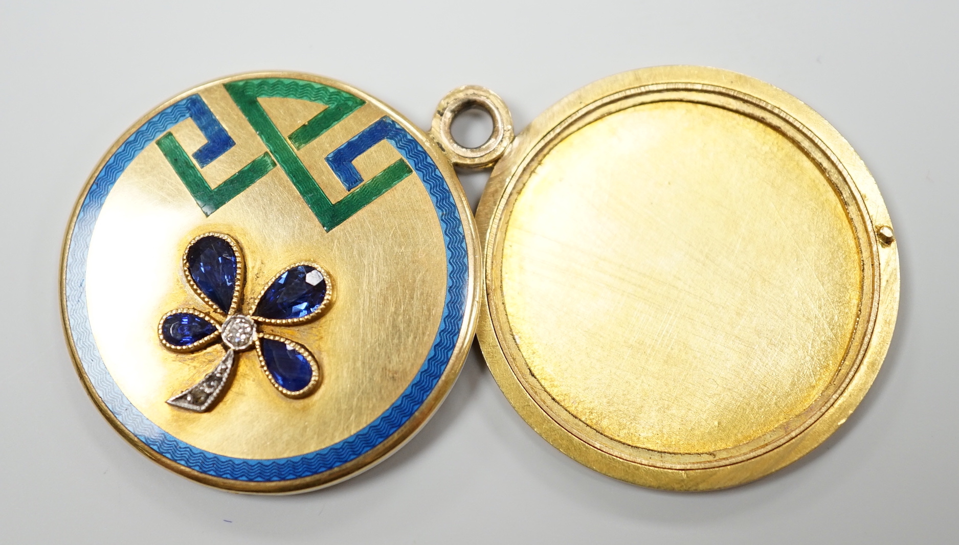 An Art Deco yellow metal, three colour enamel, synthetic? sapphire and diamond set circular locket, with clover motif, diameter 29mm